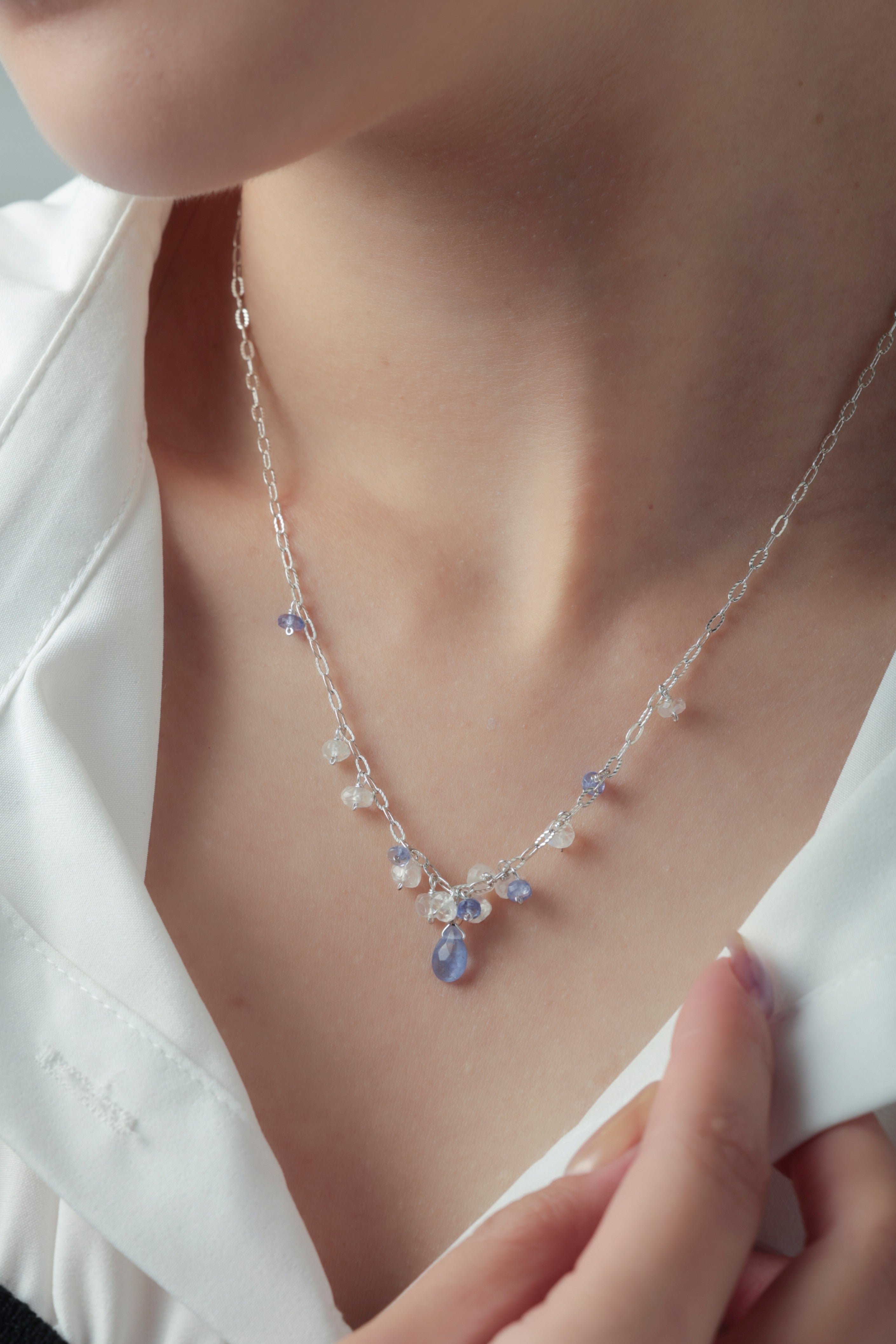 タンザナイト ネックレスの着用イメージ。白シャツの襟元で揺れる青紫の天然石が、知的でクールな印象を与えるスタイル。