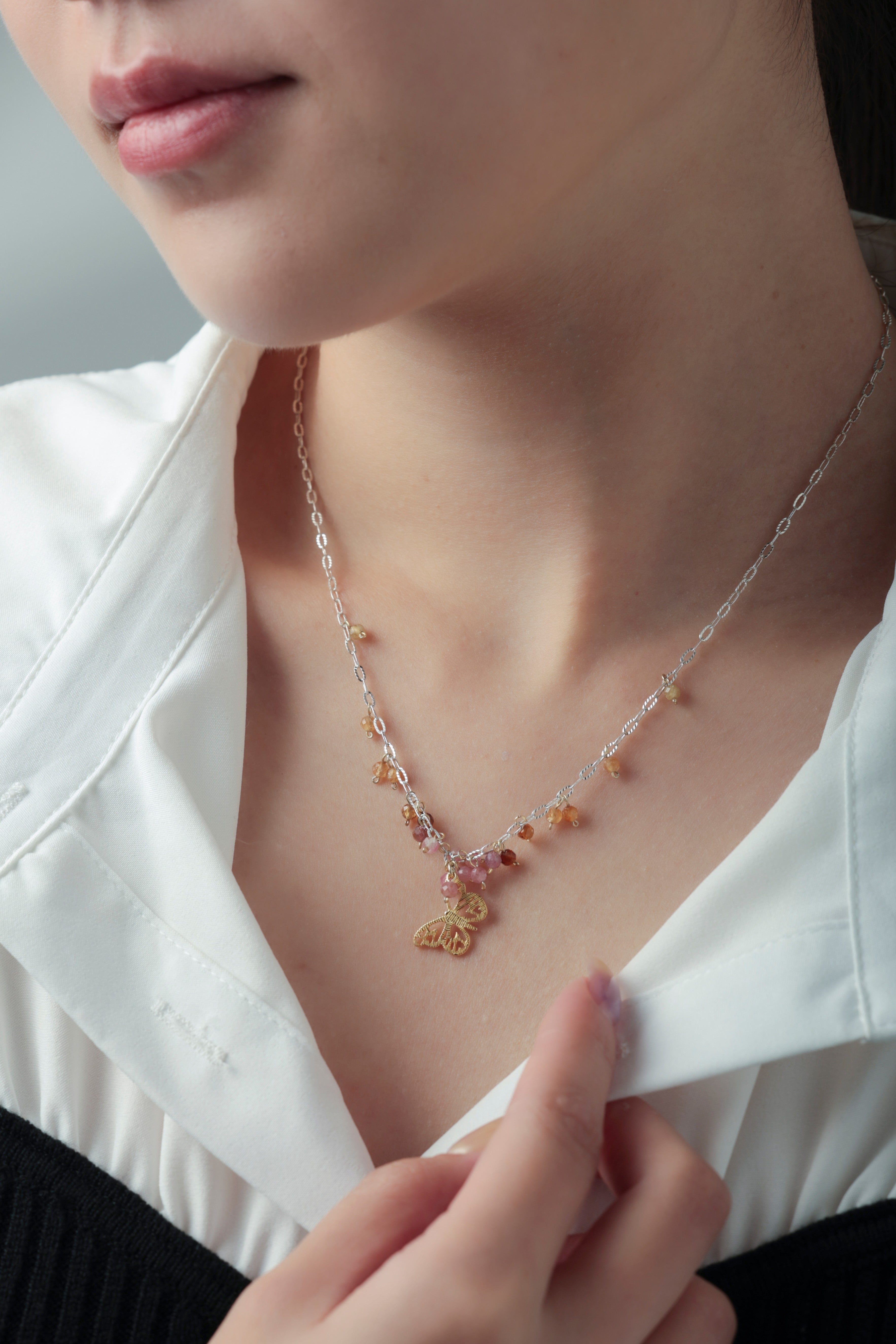 トルマリン & バタフライネックレスの着用イメージ。白シャツの襟元で揺れる金の蝶と天然石が、可憐で華やかな印象を与えるスタイル。