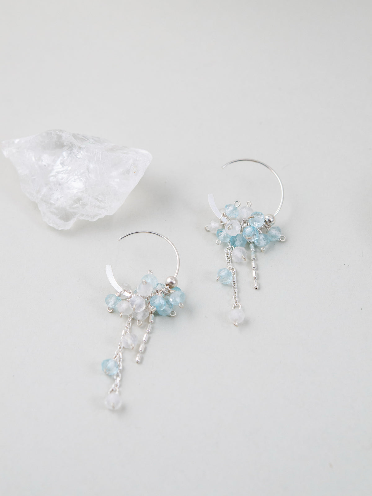 水晶と共に置かれたピアス。【水の泡】のテーマ通り、瑞々しい質感を持つ天然石のペア画像。