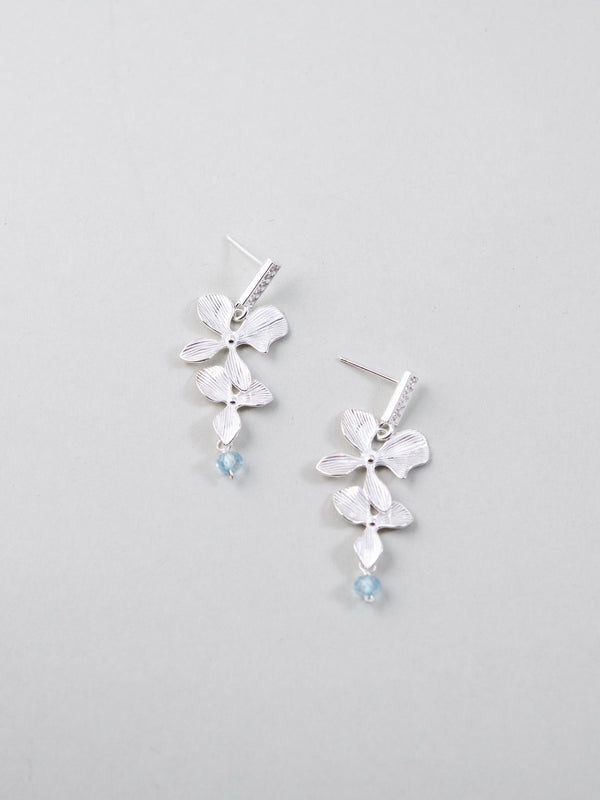 2連フラワーモチーフ & クリスタル ピアス - 【優雅な花重ね】。テクスチャー加工された2つの花が連なり、ブルーのクリスタルが揺れるSV925製耳飾り。