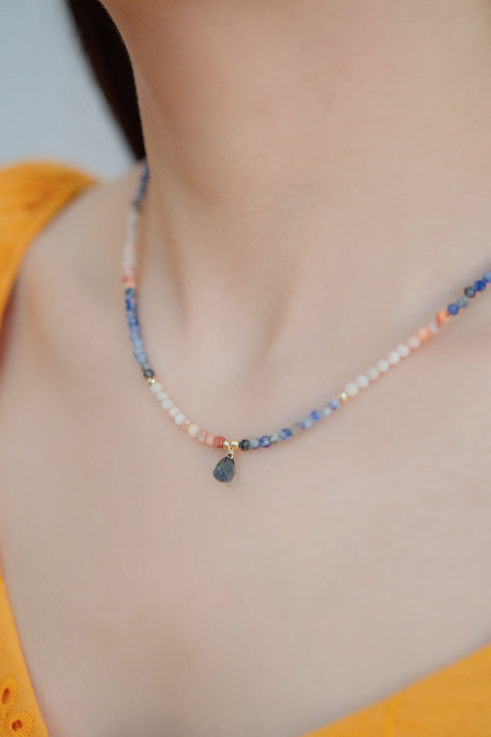 カイヤナイト ネックレスの着用イメージ。イエローのトップスに映える、深いブルーとピンクのコントラストが美しい「黄昏色」のデザイン。