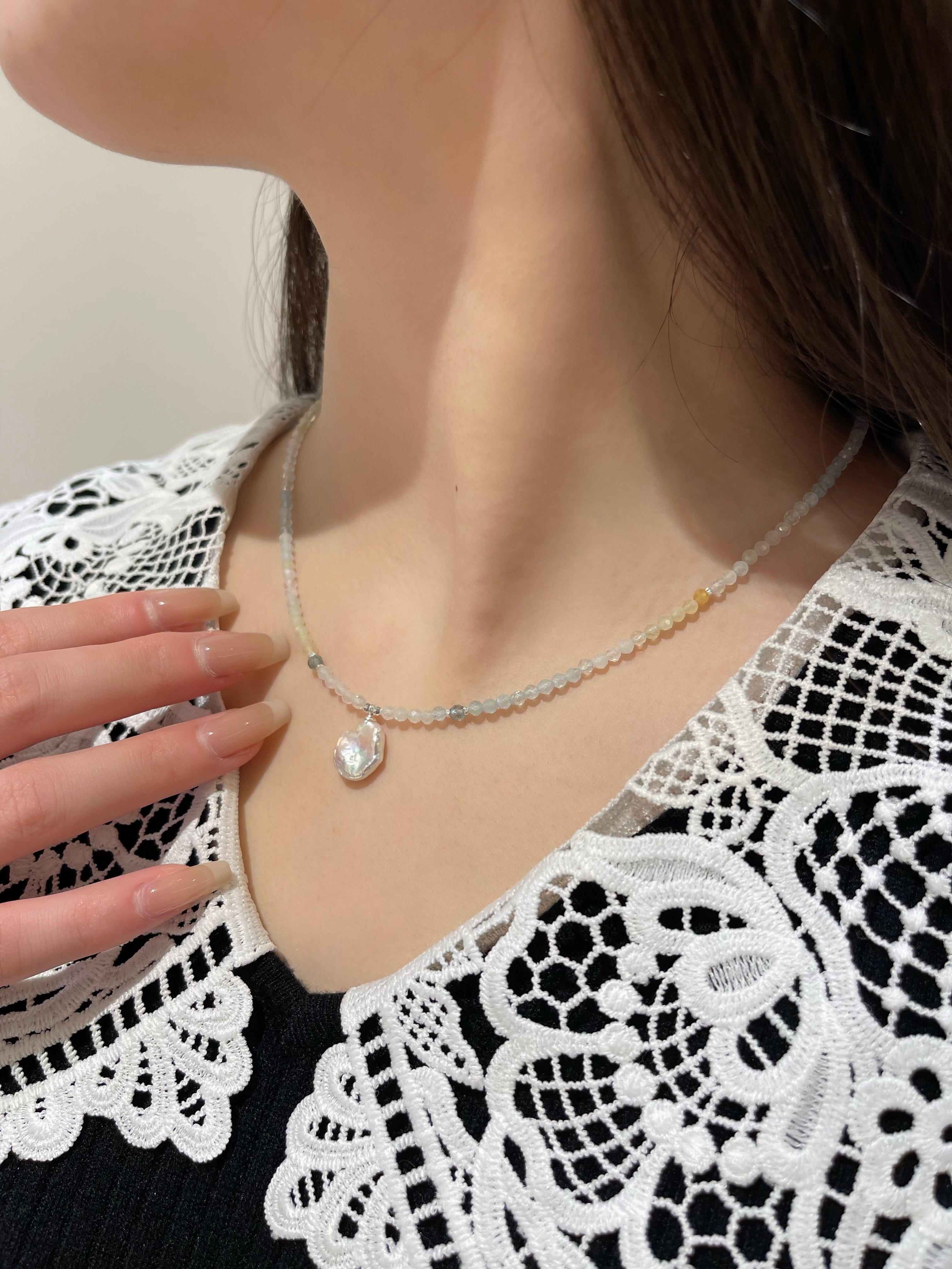 黒のレーストップスに合わせた着用イメージ。淡いブルーと白のネックレスが、シックな装いに清楚な輝きを添えるスタイル。