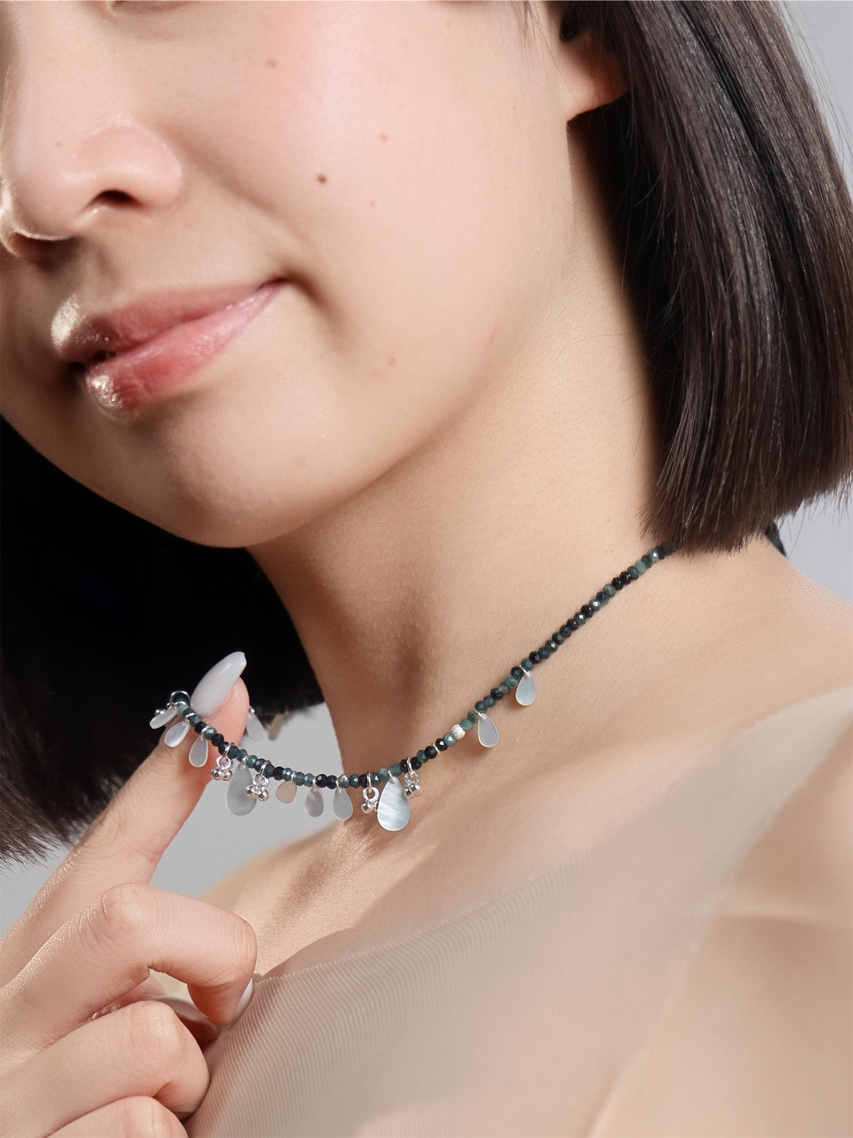 濃い緑の粒に白い貝のしずくが下がるネックレスの着用イメージ
