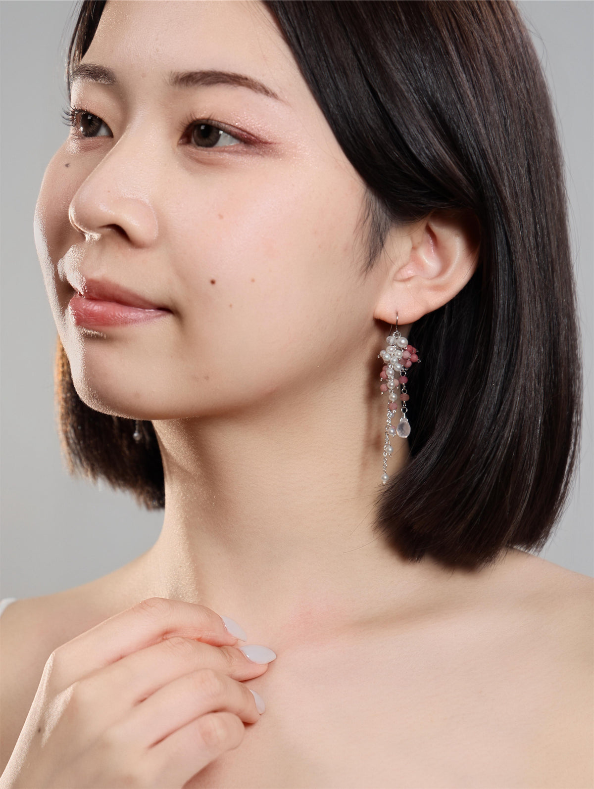 首もとに手を添えたモデルの耳もとで揺れるピアス